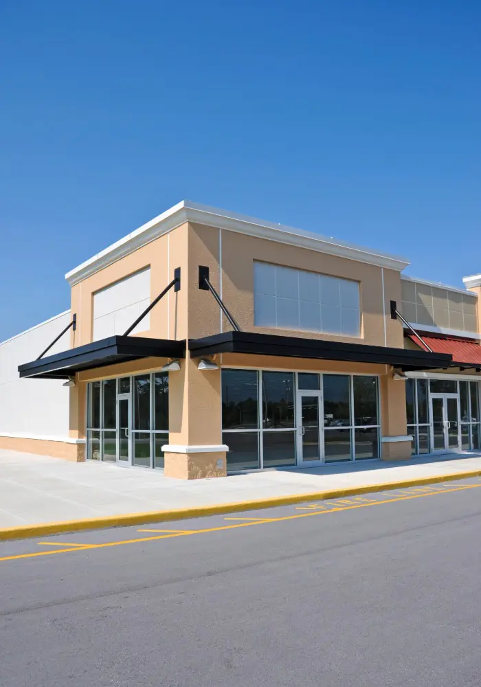 Modern commercial storefront featuring fresh beige stucco and black metal awnings expertly finished by 1st Coast Painting under a clear blue sky.