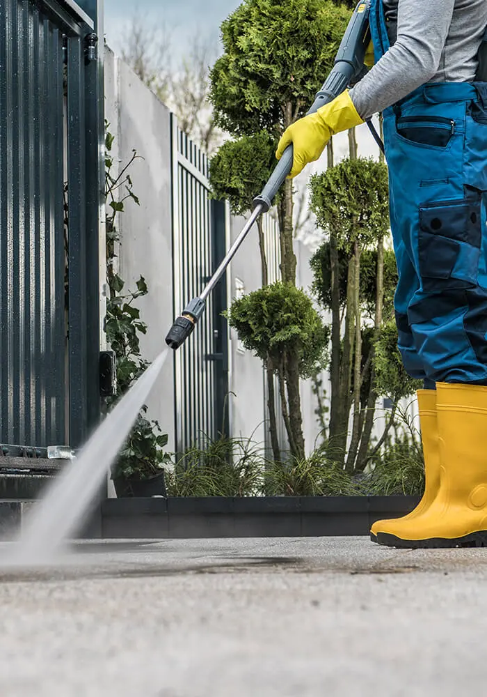 Professional technician from 1st Coast Painting using a high-pressure washer to deep clean a concrete driveway and exterior gate.