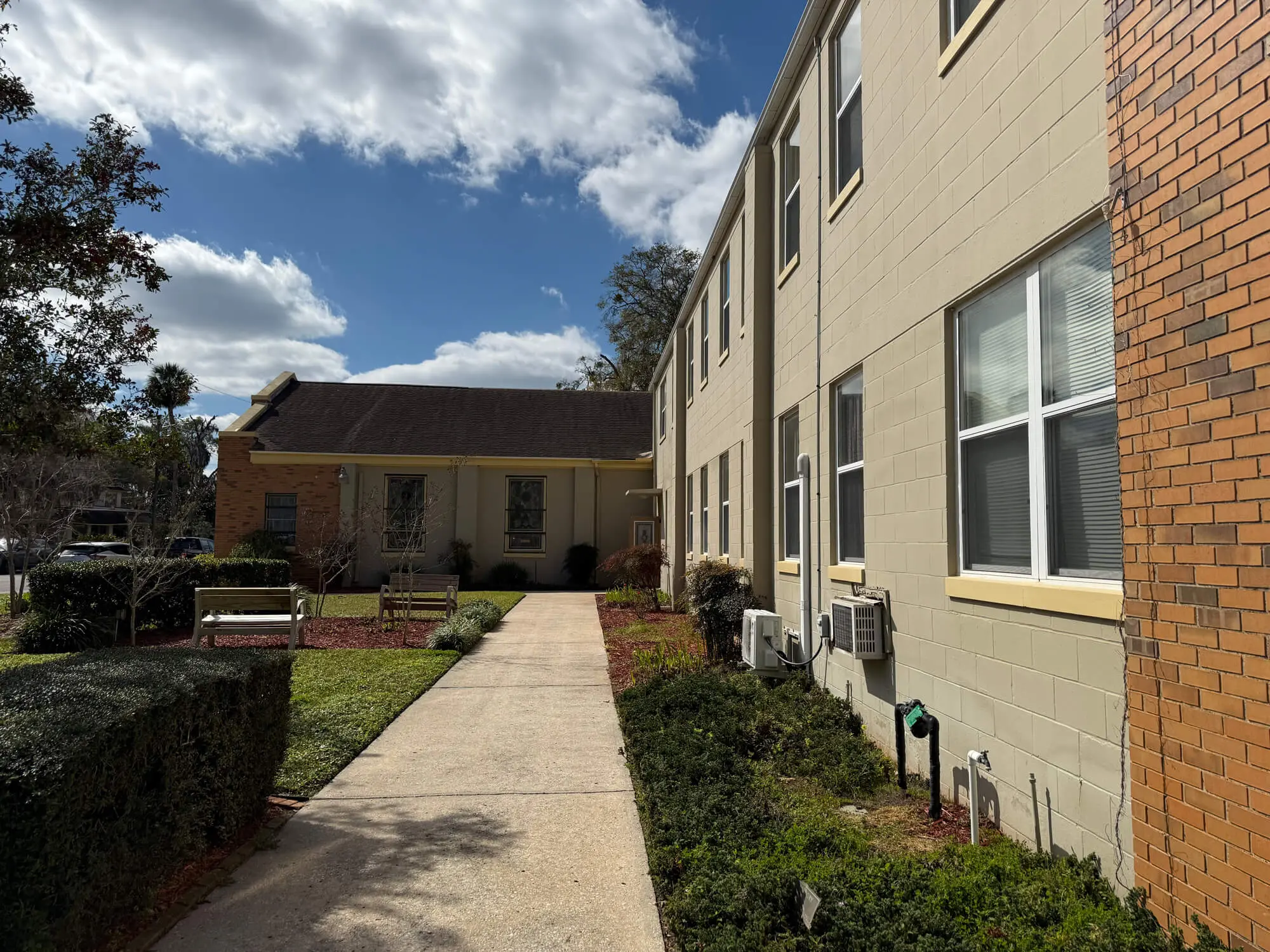 Professional commercial facility maintenance and exterior painting of a tan concrete block building and brick walkway by 1st Coast Painting.