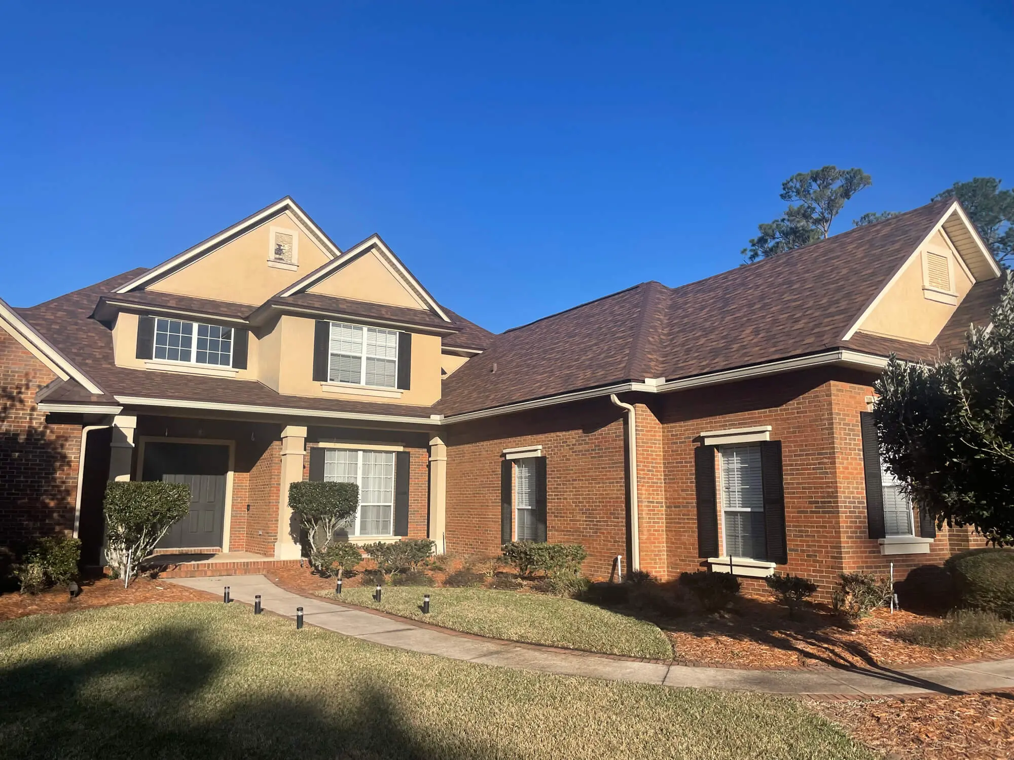 Large suburban residence featuring a red brick and tan stucco exterior with dark shutters and trim expertly painted by 1st Coast Painting.