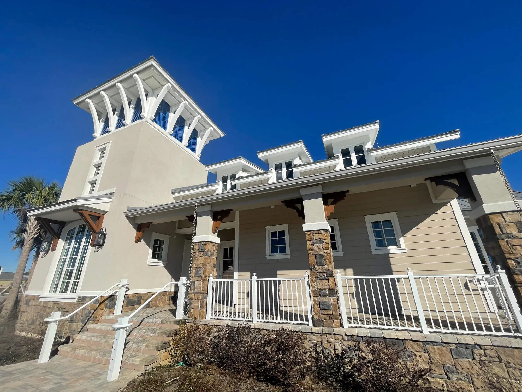 Stunning coastal architecture featuring a multi-level tan exterior with crisp white trim and stone accents expertly detailed by 1st Coast Painting.