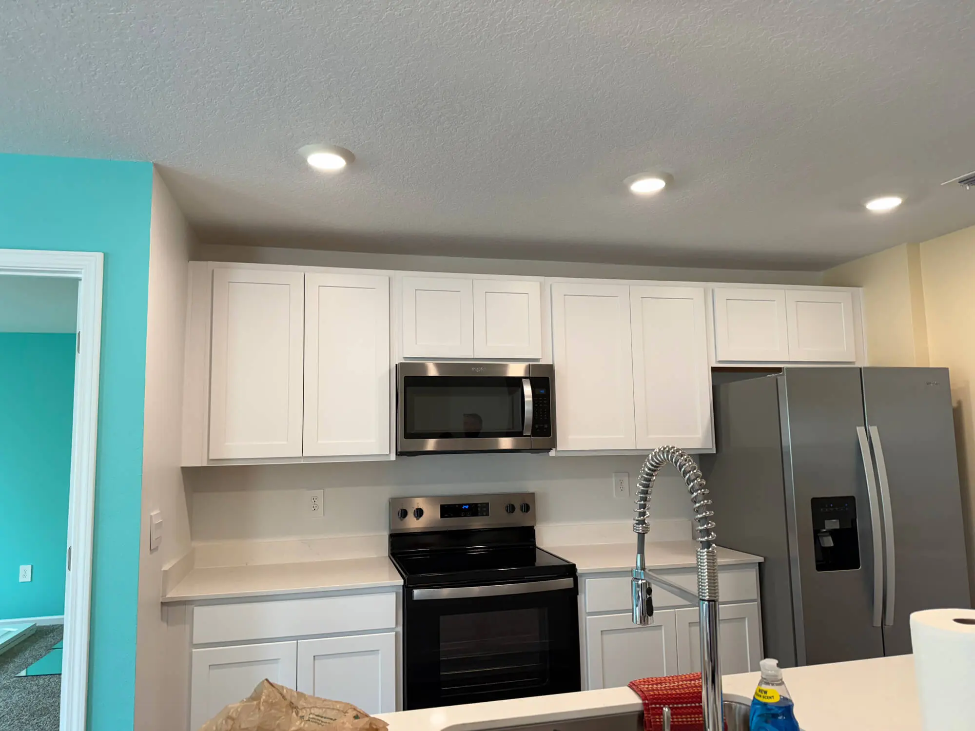 Modern kitchen renovation by 1st Coast Painting featuring vibrant turquoise accent walls, crisp white shaker cabinets, and integrated stainless steel appliances.