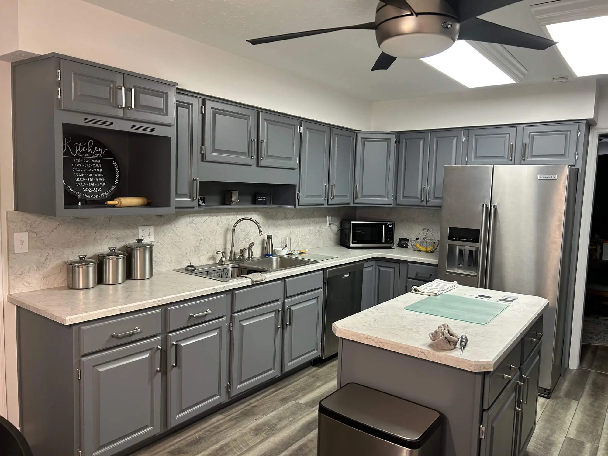 Expert cabinet refinishing by 1st Coast Painting featuring sleek charcoal grey cupboards, marbled countertops, and a matching kitchen island.