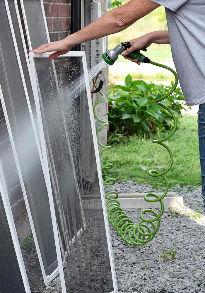 Expert 1st Coast Painting technician performs a thorough exterior house prep by deep cleaning mesh window screens with a high-pressure garden hose spray.