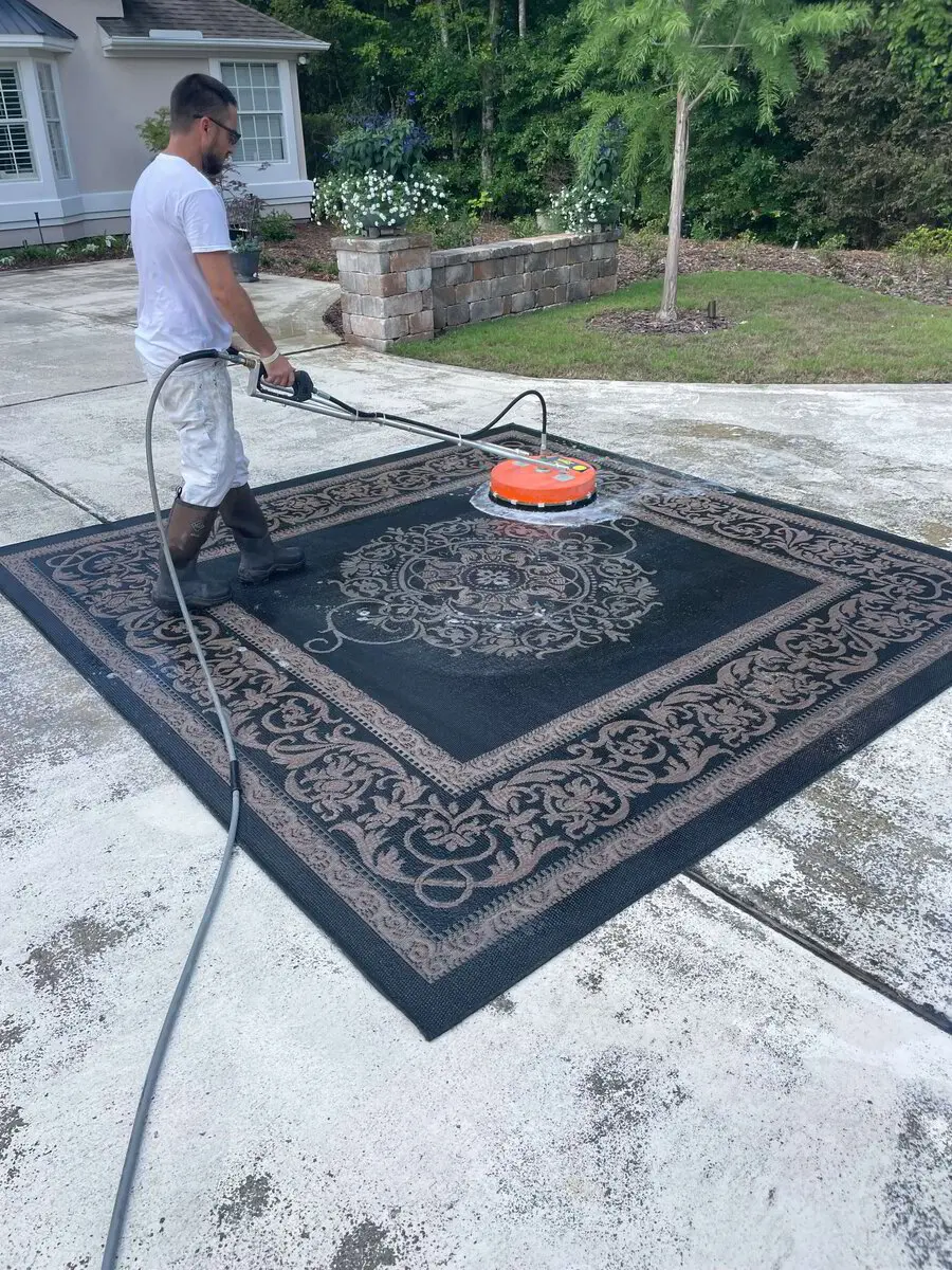 Professional exterior surface cleaning by 1st Coast Painting using a high-pressure rotary cleaner to restore a large patterned outdoor rug.