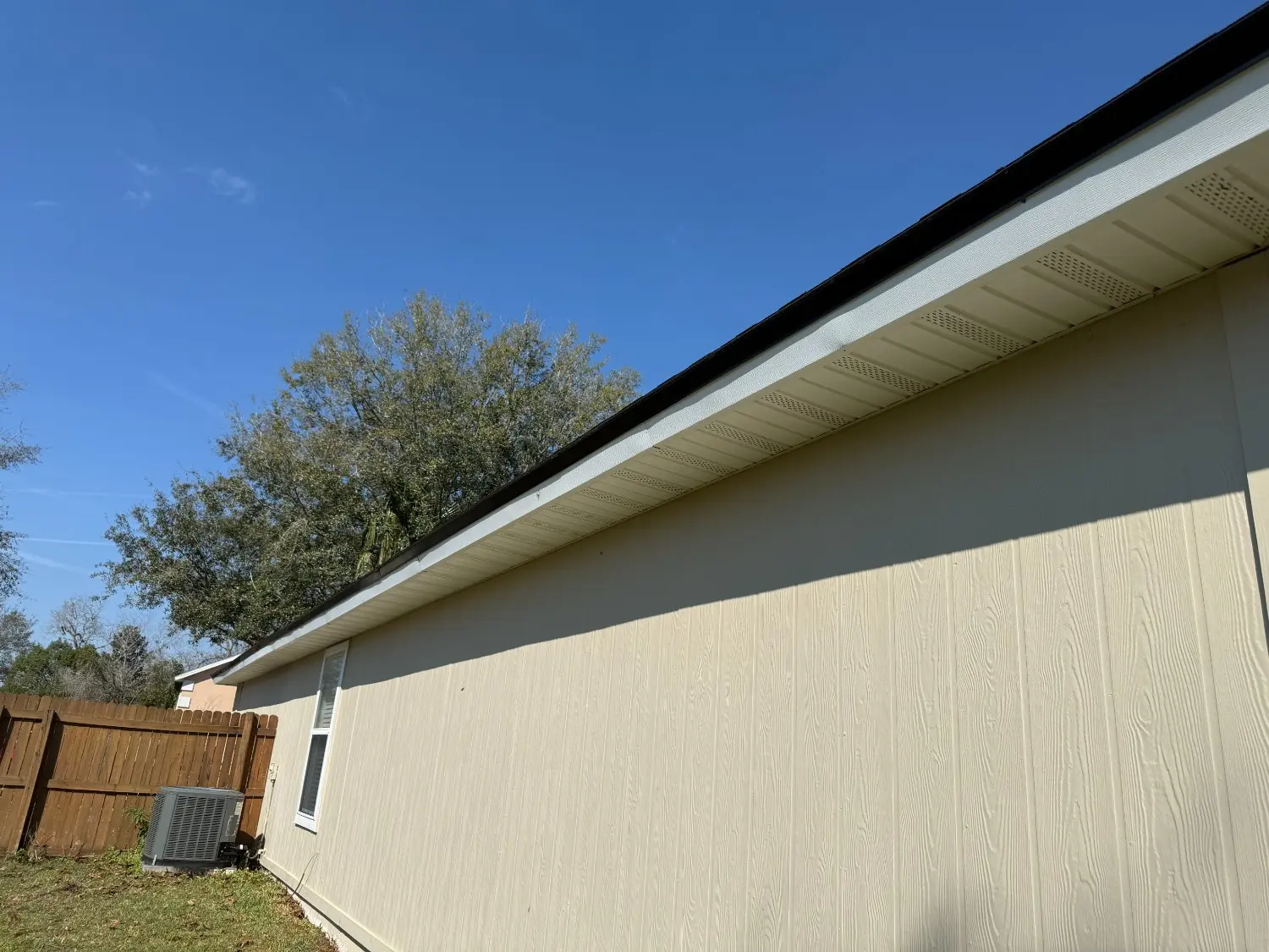 Freshly painted residential soffit, fascia, and tan wood-textured siding meticulously completed by 1st Coast Painting under a clear blue sky.