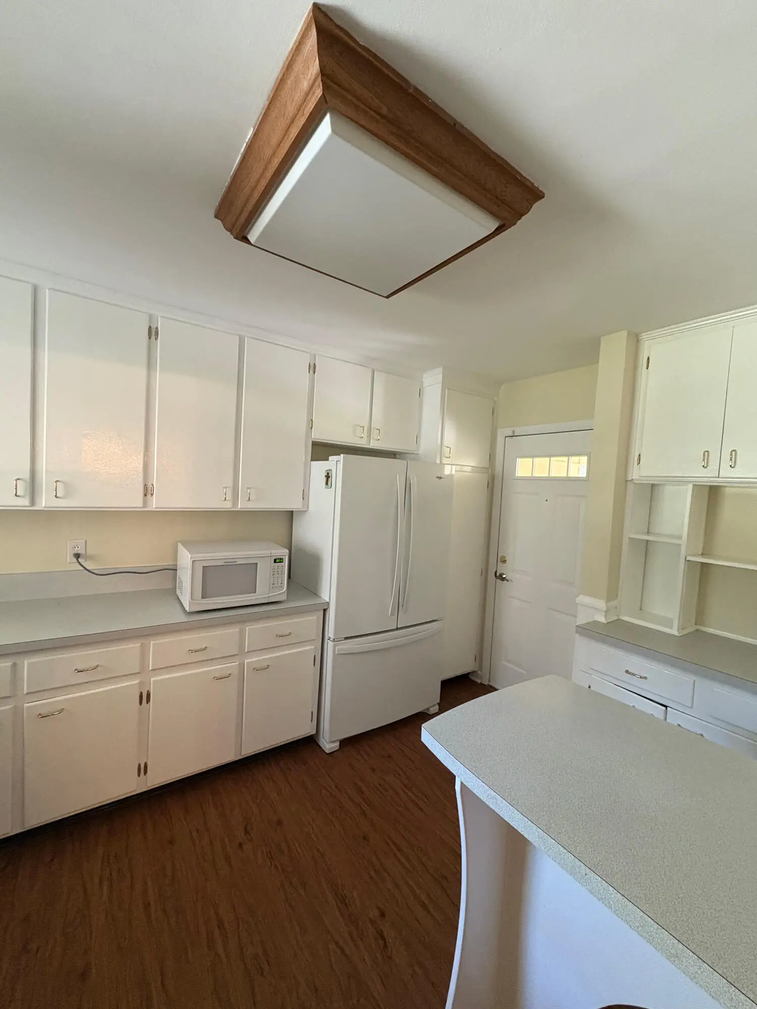 A professional team from 1st Coast Painting provides high-quality updates to this kitchen, featuring fresh white cabinetry, a wood-trimmed ceiling light, and clean laminate countertops.