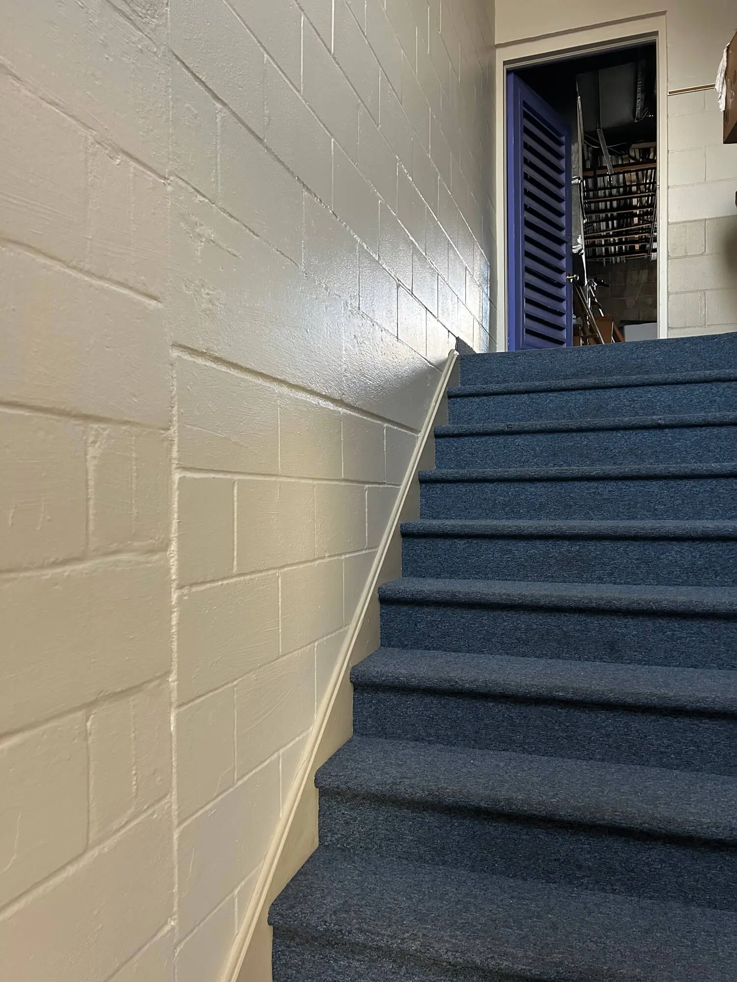 Interior staircase featuring blue carpet and glossy cream-colored masonry block walls, reflecting the high-quality commercial coating standards of 1st Coast Painting.
