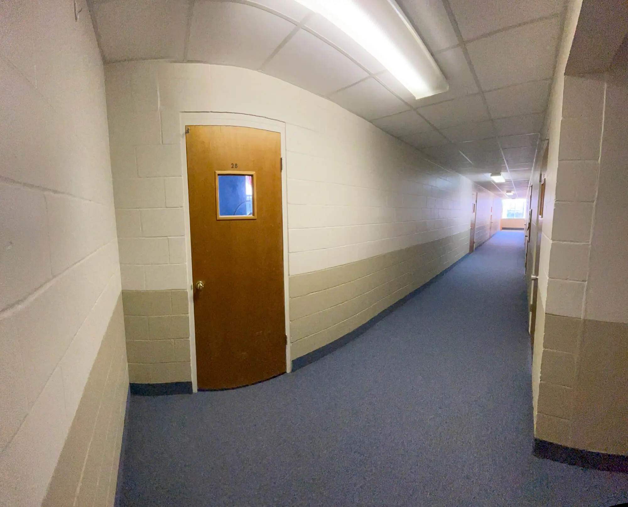 A curved institutional hallway featuring two-tone neutral cinder block walls and a wood grain door, showcasing professional commercial interior finishing by 1st Coast Painting.