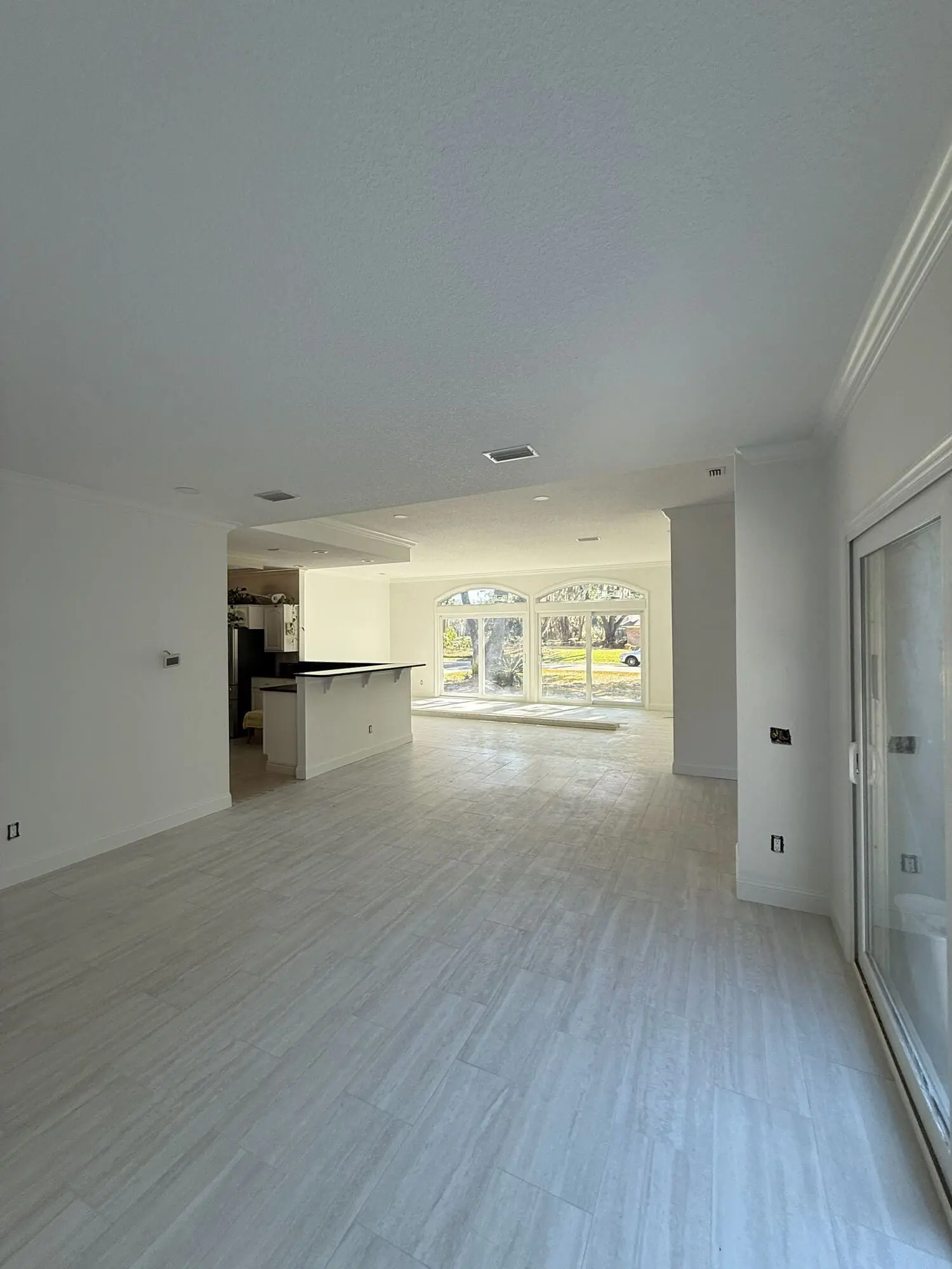 1st Coast Painting showcases a bright open-concept living space featuring crisp white walls, elegant crown molding, and seamless transitions between the kitchen and sunlit sliding glass doors.