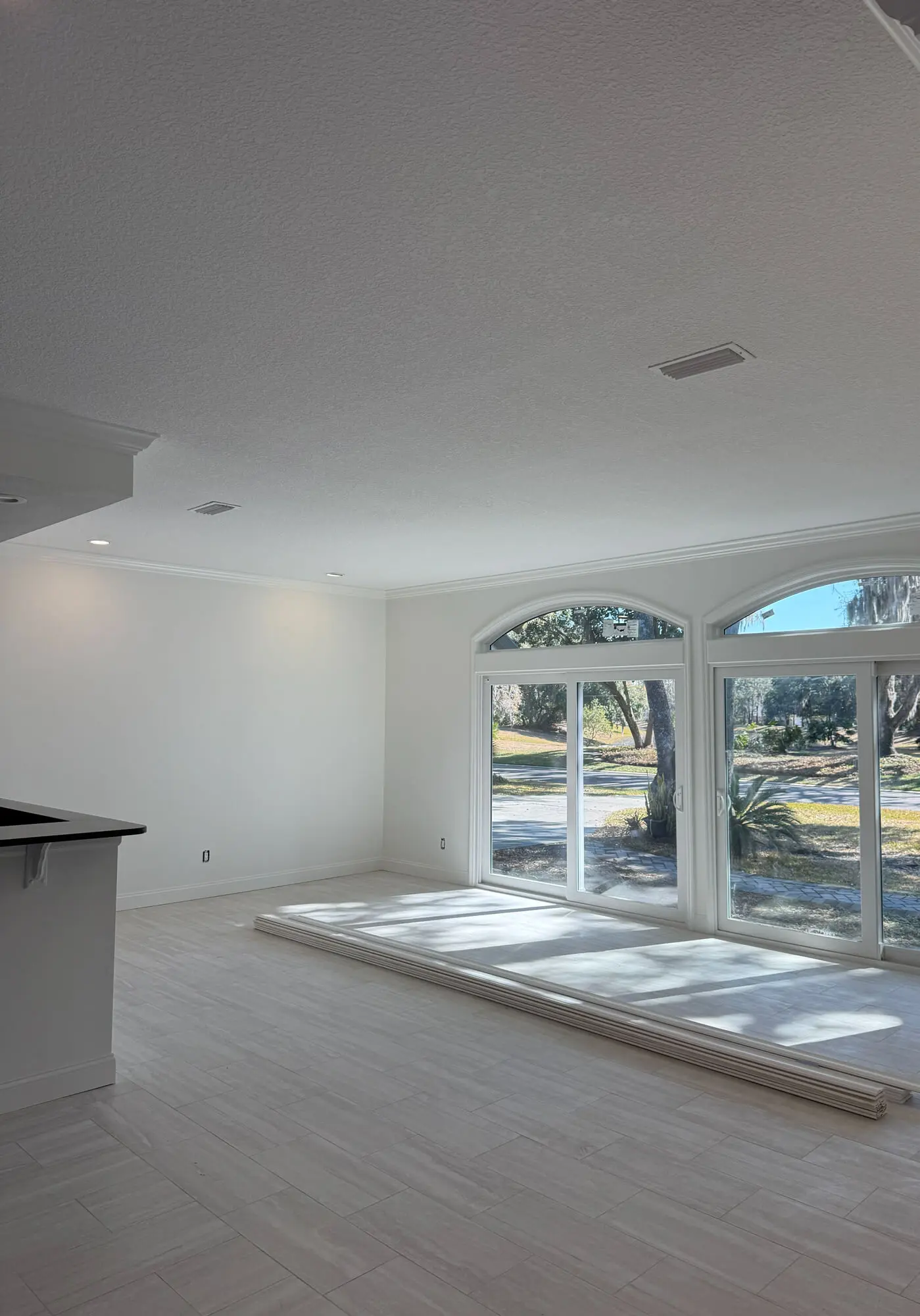 Bright open-concept room featuring white crown molding and recessed lighting, professionally finished by 1st Coast Painting to enhance natural light from large arched windows.