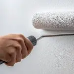 A painter rolling white primer on an interior wall before painting.