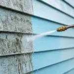 A pressure washer removing dirt and mold from a house exterior before painting.