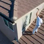 A painter applying primer to an exterior stucco wall during surface preparation for a house painting project