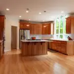 Kitchen with warm wood-tone cabinetry, a central island, and hardwood floors, showing what cabinet refinishing and its benefits look like in a finished space.