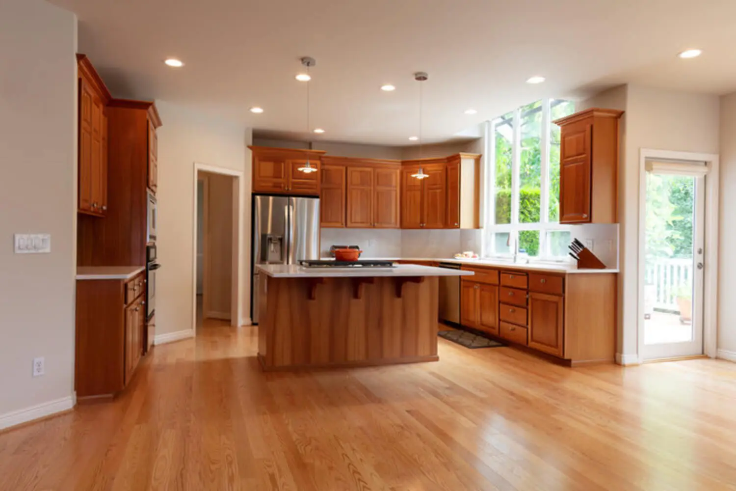 Kitchen with warm wood-tone cabinetry, a central island, and hardwood floors, showing what cabinet refinishing and its benefits look like in a finished space.