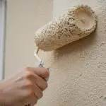 Roller applying light exterior paint to a stucco wall in mild, dry weather, illustrating the best time of year for exterior house painting.
