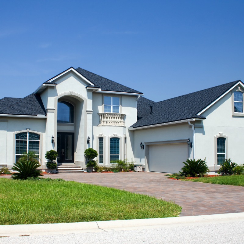 Stately white stucco luxury home with a dark shingle roof and arched entryway, showcasing premium exterior finishes by 1st Coast Painting.