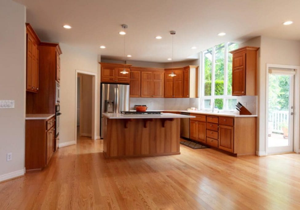 Kitchen with warm wood-tone cabinetry, a central island, and hardwood floors, showing what cabinet refinishing and its benefits look like in a finished space.
