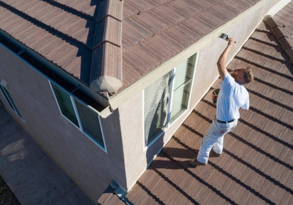 A painter applying primer to an exterior stucco wall during surface preparation for a house painting project